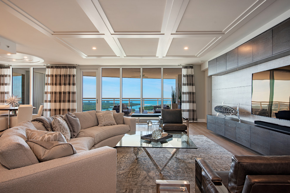 На фото: открытая гостиная комната в морском стиле с серыми стенами, паркетным полом среднего тона, телевизором на стене и коричневым полом с
