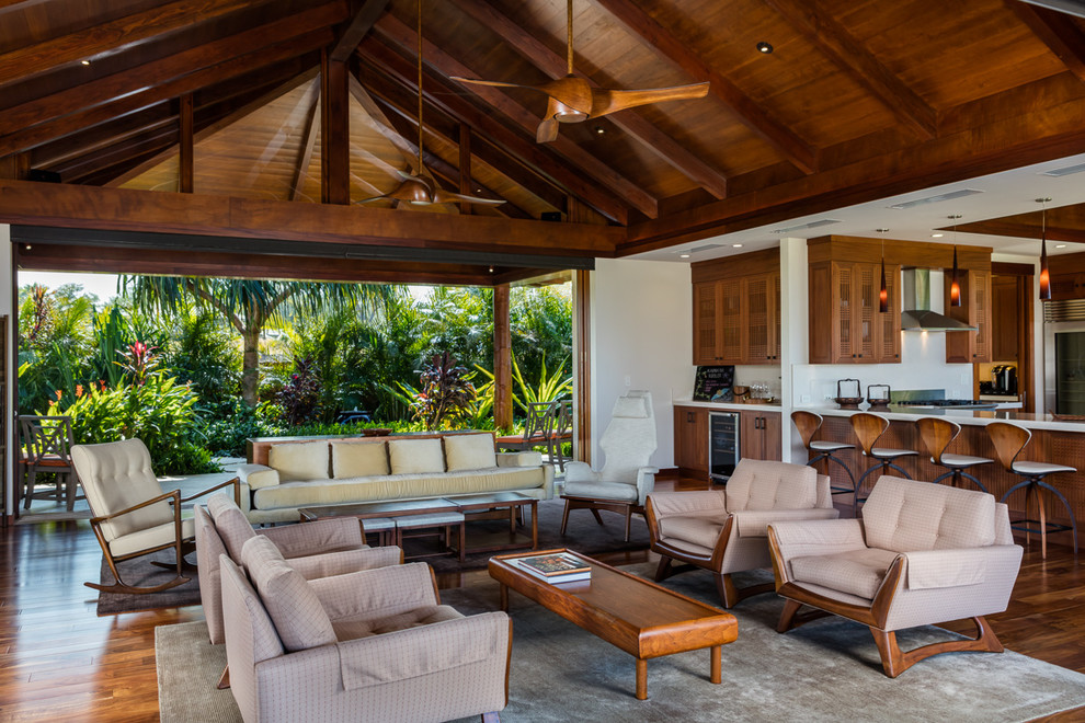 Foto de salón para visitas abierto tropical de tamaño medio sin chimenea y televisor con suelo de madera en tonos medios, paredes beige y alfombra