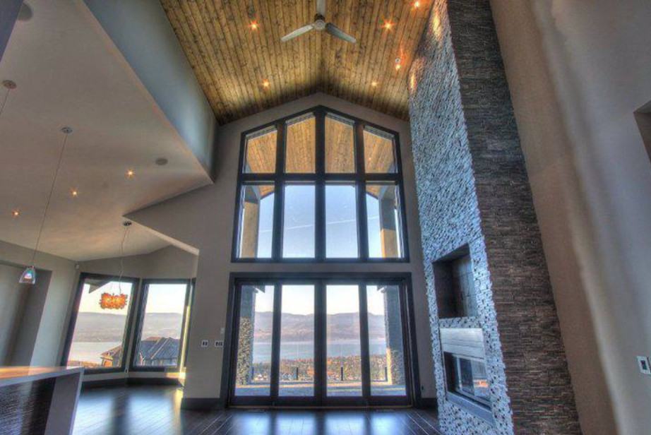 Foto de salón abierto actual grande con paredes grises, suelo de madera en tonos medios, chimenea lineal, marco de chimenea de piedra y pared multimedia