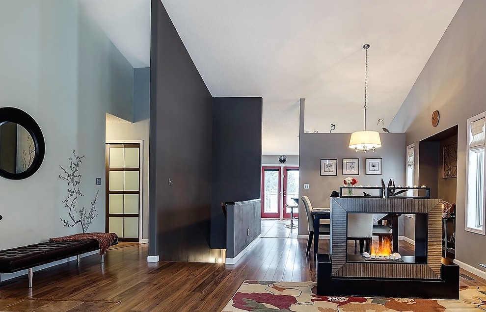 Пример оригинального дизайна: гостиная комната в современном стиле с серыми стенами, полом из ламината, двусторонним камином, фасадом камина из металла и разноцветным полом