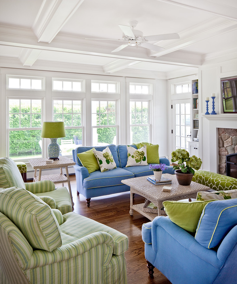 Example of a beach style enclosed medium tone wood floor and brown floor living room design in Portland Maine with white walls, a stone fireplace and a wall-mounted tv