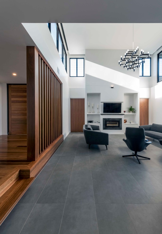 Стильный дизайн: открытая гостиная комната в современном стиле с белыми стенами, полом из керамической плитки, стандартным камином, фасадом камина из плитки, телевизором на стене и серым полом - последний тренд