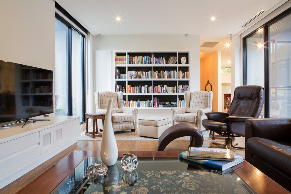 Imagen de biblioteca en casa abierta minimalista de tamaño medio con paredes blancas, suelo de madera en tonos medios y televisor independiente