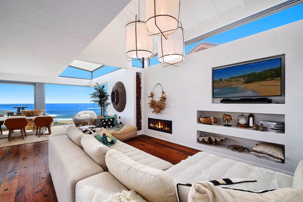 На фото: открытая гостиная комната в морском стиле с белыми стенами, темным паркетным полом, горизонтальным камином, телевизором на стене и коричневым полом с