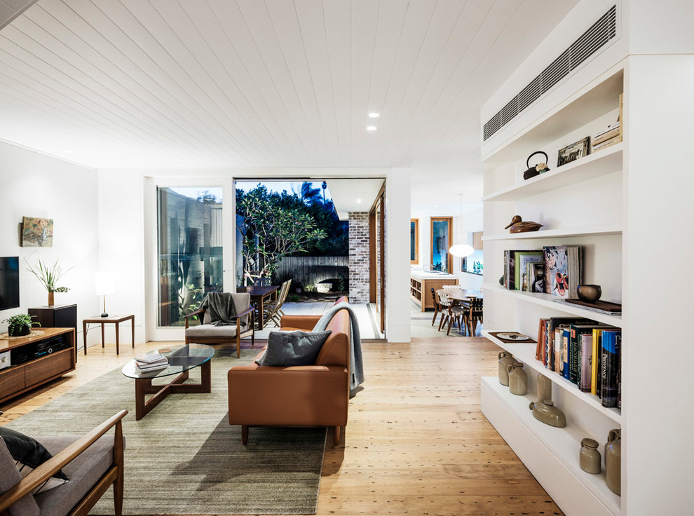 Modelo de salón para visitas abierto contemporáneo con paredes blancas, suelo de madera en tonos medios, suelo beige y televisor colgado en la pared
