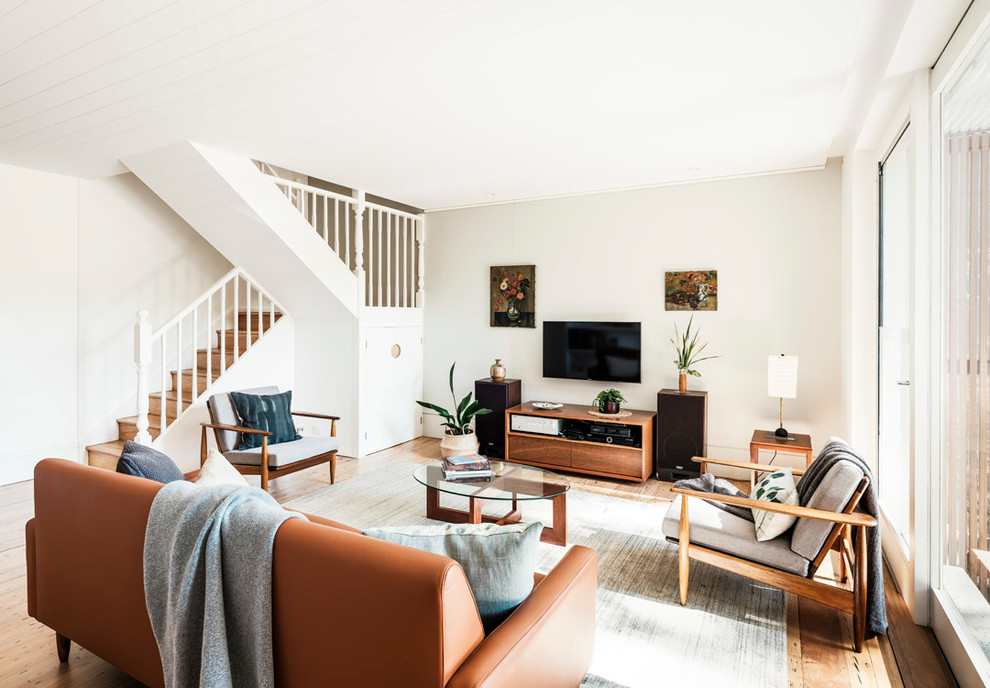 Modelo de salón abierto contemporáneo de tamaño medio sin chimenea con paredes blancas, suelo de madera clara, televisor colgado en la pared y suelo beige