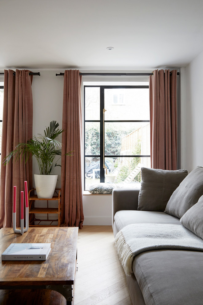 This is an example of a medium sized contemporary open plan living room in London with white walls and light hardwood flooring.