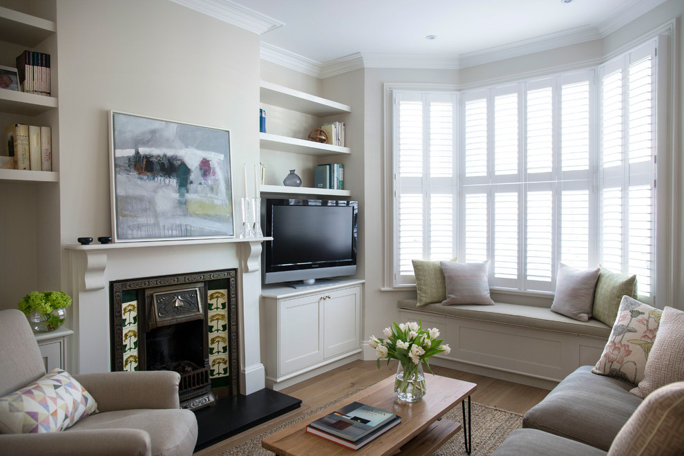 Cette photo montre un petit salon tendance fermé avec un mur beige, parquet clair, une cheminée standard, un manteau de cheminée en bois et un téléviseur encastré.