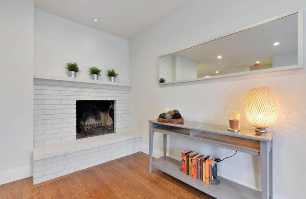 This is an example of a contemporary enclosed living room in Boston with white walls, medium hardwood flooring, a standard fireplace, a brick fireplace surround and no tv.