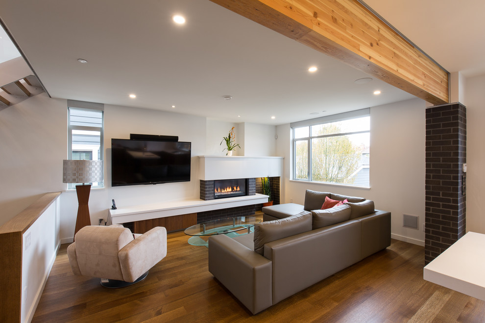 Design ideas for a large contemporary open plan living room in Vancouver with white walls, light hardwood flooring, a standard fireplace, a brick fireplace surround and a wall mounted tv.