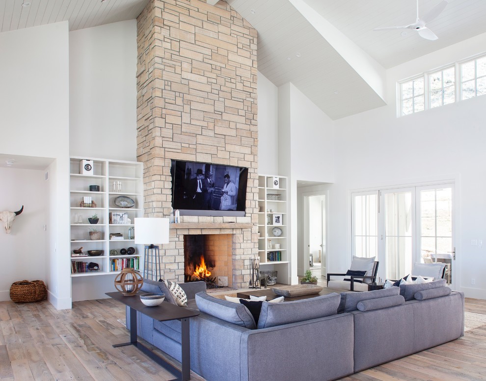 Offenes Landhaus Wohnzimmer mit weißer Wandfarbe, braunem Holzboden, Kamin, Kaminumrandung aus Stein, TV-Wand und braunem Boden in Denver