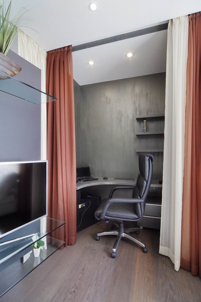 Пример оригинального дизайна: маленькая гостиная комната в современном стиле с с книжными шкафами и полками, серыми стенами, отдельно стоящим телевизором, коричневым полом и тюлем на окнах для на участке и в саду