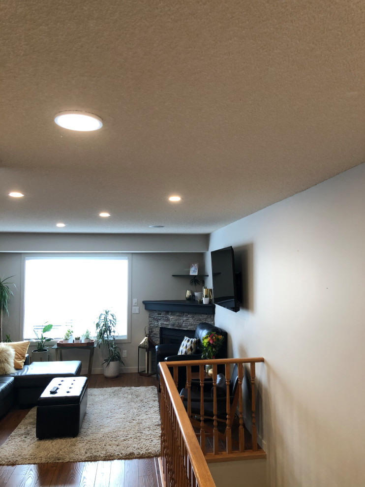Mittelgroßes, Abgetrenntes Modernes Wohnzimmer mit beiger Wandfarbe, hellem Holzboden, Eckkamin, Kaminumrandung aus Stein, TV-Wand und gelbem Boden in Edmonton