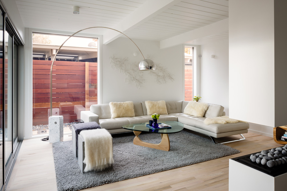 На фото: гостиная комната в стиле модернизм с белыми стенами, светлым паркетным полом и двусторонним камином