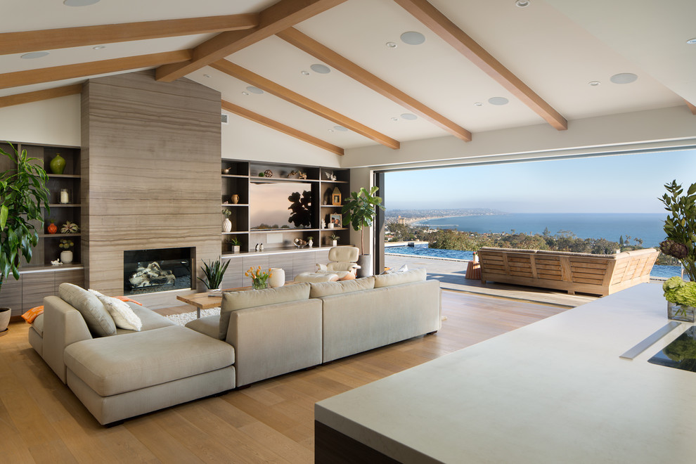 サンディエゴにある広いビーチスタイルのおしゃれなLDK (白い壁、淡色無垢フローリング、標準型暖炉、石材の暖炉まわり、壁掛け型テレビ、茶色い床) の写真