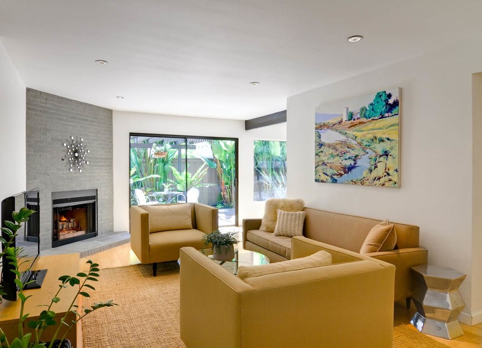 Стильный дизайн: гостиная комната в современном стиле с белыми стенами, угловым камином и горчичным диваном - последний тренд