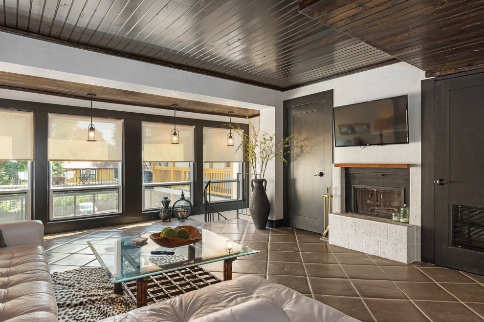 На фото: открытая гостиная комната среднего размера в стиле фьюжн с белыми стенами, полом из терракотовой плитки, стандартным камином, фасадом камина из плитки, телевизором на стене, коричневым полом и деревянным потолком