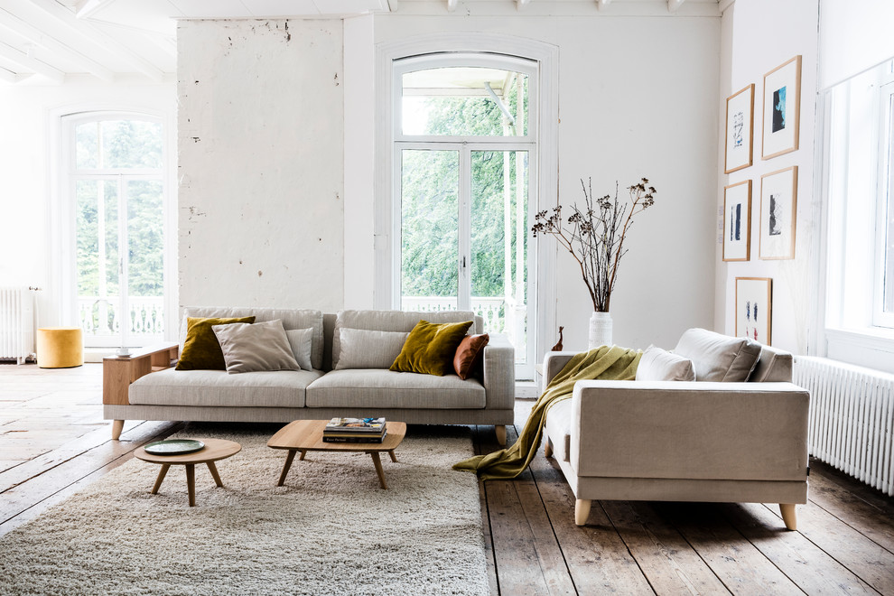 Modelo de salón para visitas abierto escandinavo con paredes blancas, suelo de madera en tonos medios y suelo marrón
