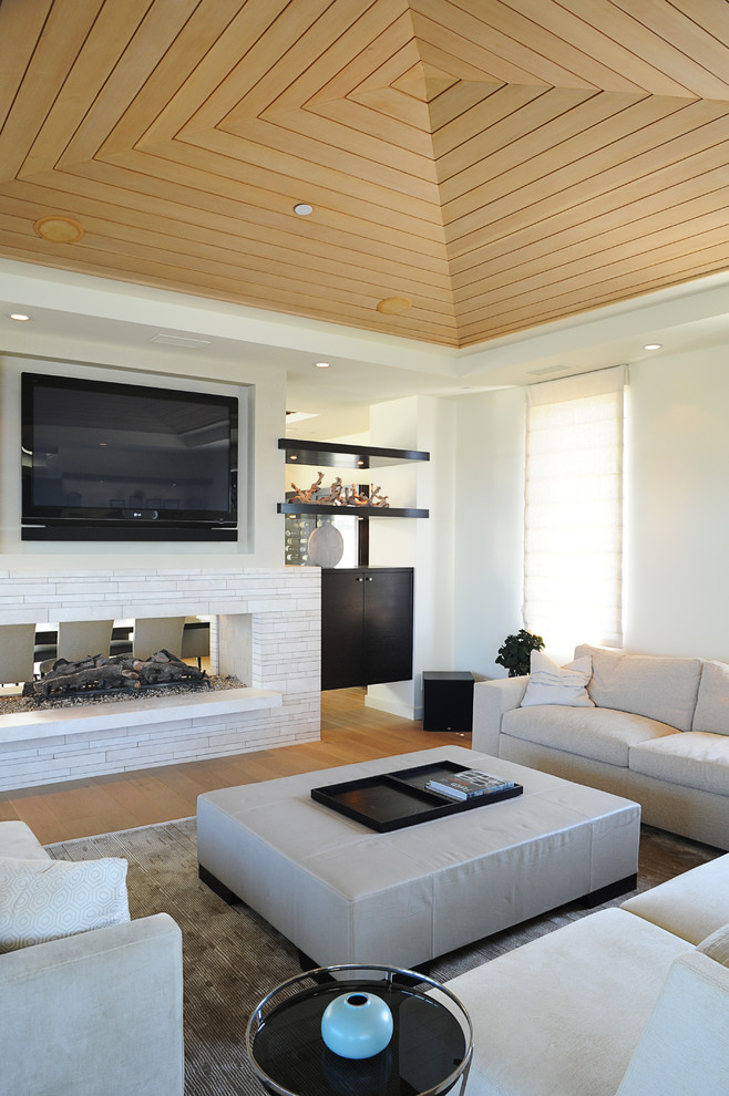 Cette image montre un salon marin avec un mur blanc, une cheminée double-face et un téléviseur fixé au mur.
