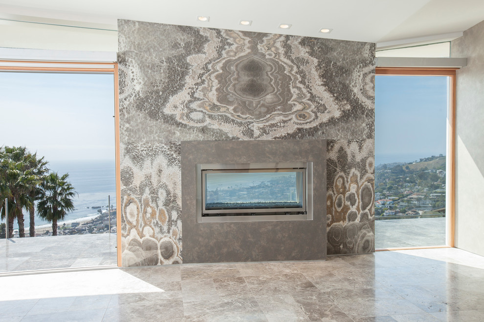 На фото: большая открытая гостиная комната в современном стиле с серыми стенами, мраморным полом, двусторонним камином и фасадом камина из камня с