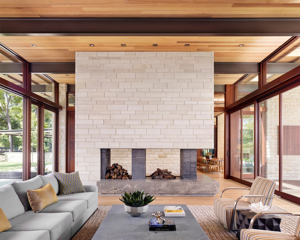 Inspiration for a contemporary living room in Austin with a two-sided fireplace, a stone fireplace surround and beige floors.