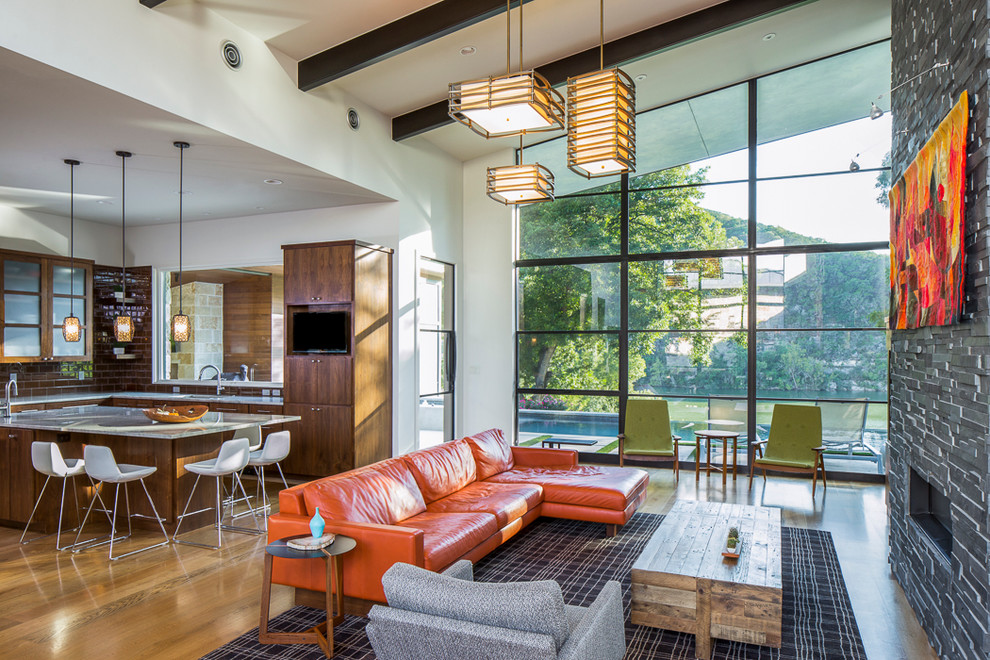 Offenes Modernes Wohnzimmer mit weißer Wandfarbe, braunem Holzboden, Gaskamin und Kaminumrandung aus Stein in Austin
