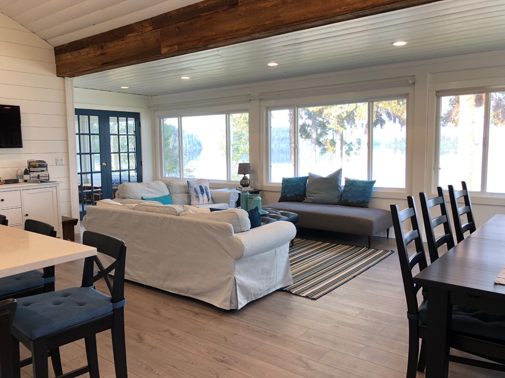 他の地域にある低価格の中くらいなビーチスタイルのおしゃれなLDK (白い壁、ラミネートの床、薪ストーブ、タイルの暖炉まわり、壁掛け型テレビ、グレーの床) の写真