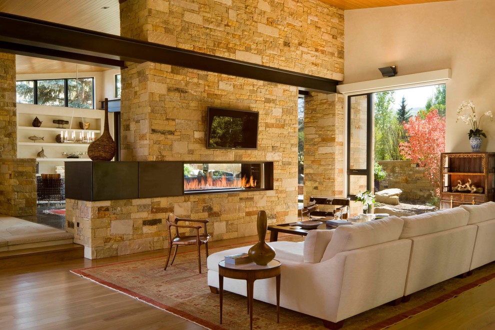 На фото: гостиная комната в современном стиле с двусторонним камином и телевизором на стене с