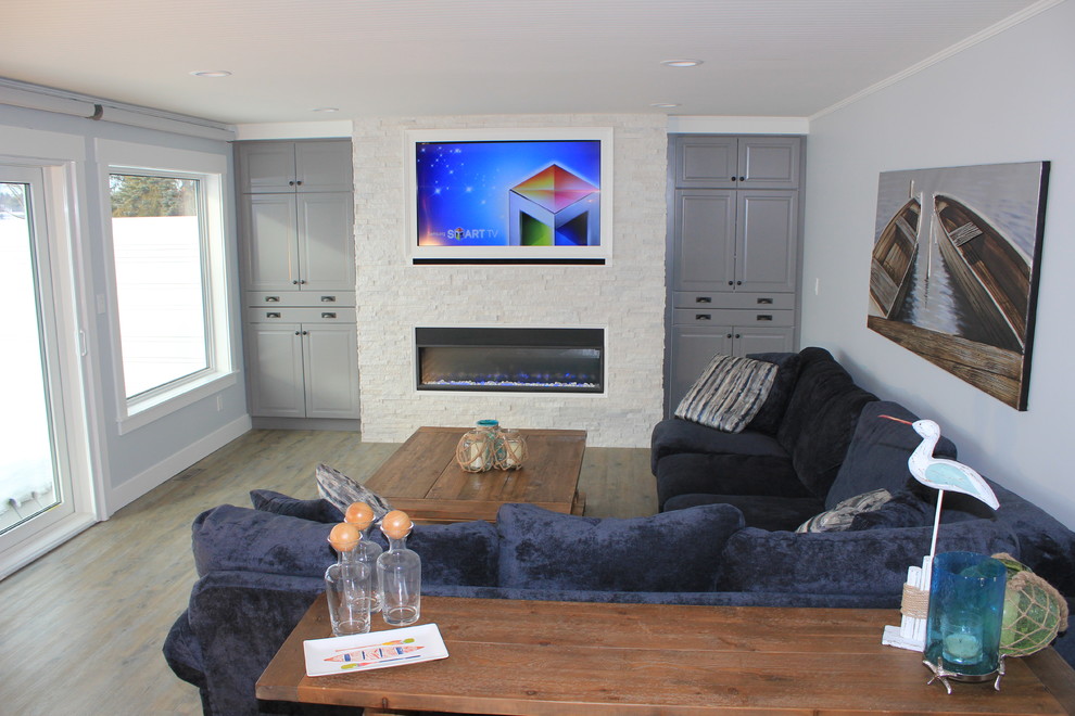 Aménagement d'un salon bord de mer de taille moyenne et ouvert avec un mur gris, un sol en vinyl, une cheminée ribbon, un manteau de cheminée en pierre et un téléviseur dissimulé.