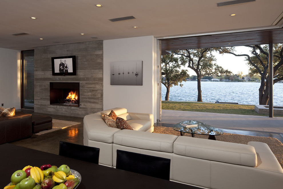 オースティンにある広いコンテンポラリースタイルのおしゃれなLDK (白い壁、標準型暖炉、コンクリートの床、コンクリートの暖炉まわり、壁掛け型テレビ) の写真