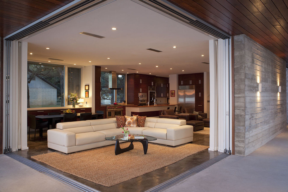 Пример оригинального дизайна: большая открытая гостиная комната в современном стиле с бетонным полом, белыми стенами, стандартным камином, фасадом камина из бетона, телевизором на стене и ковром на полу