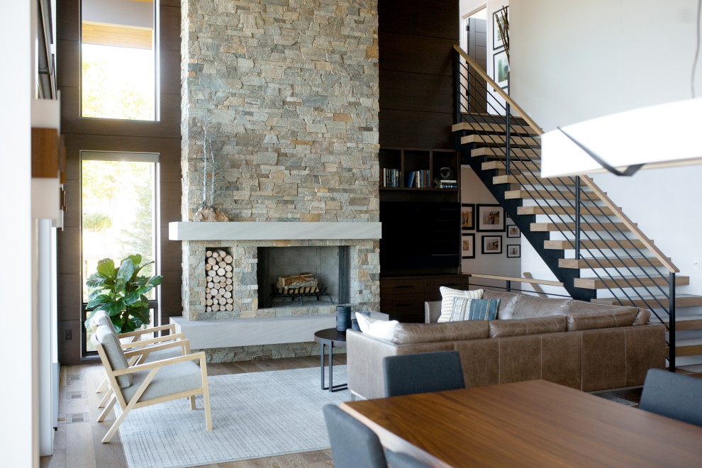Photo of a contemporary formal open plan living room in Grand Rapids with no tv, a standard fireplace, a vaulted ceiling, multi-coloured walls, medium hardwood flooring, brown floors, wood walls and a stacked stone fireplace surround.