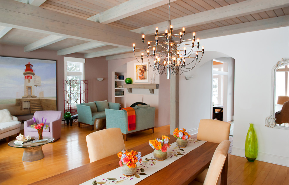 На фото: открытая гостиная комната в современном стиле с розовыми стенами, паркетным полом среднего тона, стандартным камином и балками на потолке без телевизора