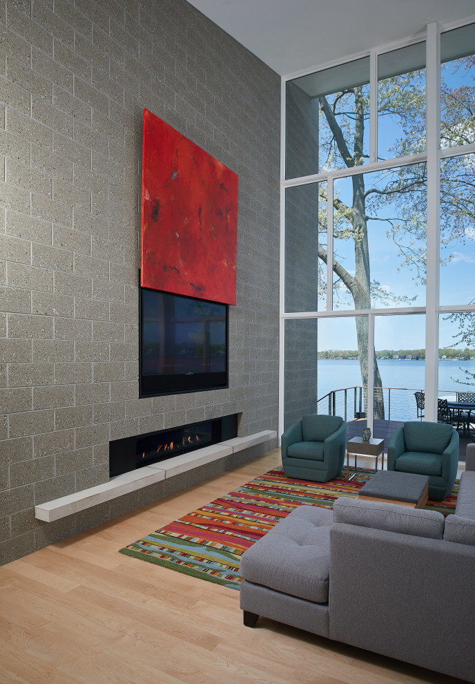 Ejemplo de salón abierto moderno con paredes grises, suelo de madera clara, chimenea lineal, marco de chimenea de ladrillo, televisor retractable y suelo marrón