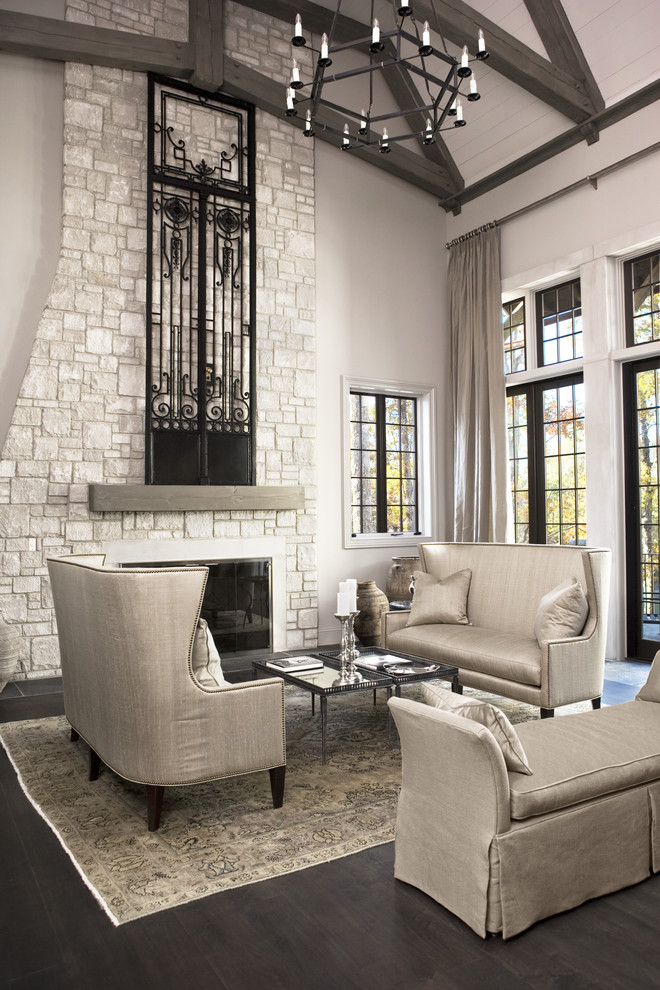Пример оригинального дизайна: большая открытая, парадная гостиная комната в стиле неоклассика (современная классика) с фасадом камина из камня, серыми стенами, темным паркетным полом, стандартным камином и ковром на полу