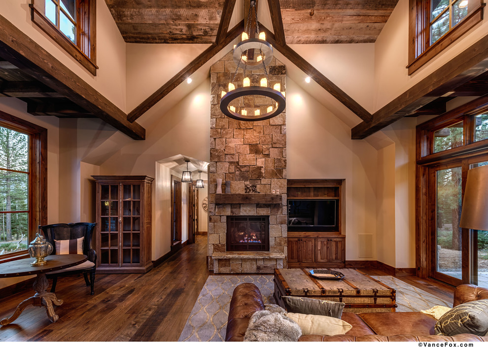 Cette image montre un grand salon minimaliste ouvert avec une salle de réception, un mur beige, un sol en bois brun, une cheminée standard, un manteau de cheminée en pierre et un téléviseur encastré.