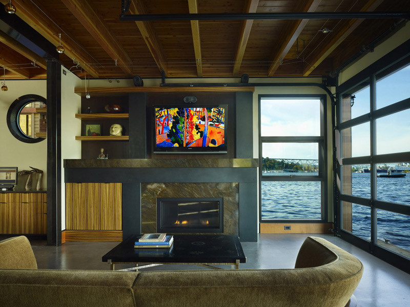 シアトルにあるラグジュアリーな小さなインダストリアルスタイルのおしゃれなLDK (ベージュの壁、標準型暖炉、石材の暖炉まわり、壁掛け型テレビ、コンクリートの床、ベージュの床) の写真