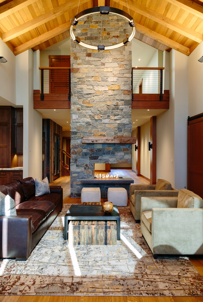 Imagen de salón para visitas abierto rural de tamaño medio sin televisor con paredes blancas, suelo de madera clara, chimenea de doble cara y marco de chimenea de piedra