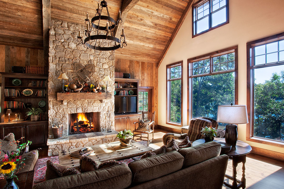 Cette image montre un salon chalet avec parquet clair, une cheminée standard, un manteau de cheminée en pierre, un téléviseur encastré et éclairage.