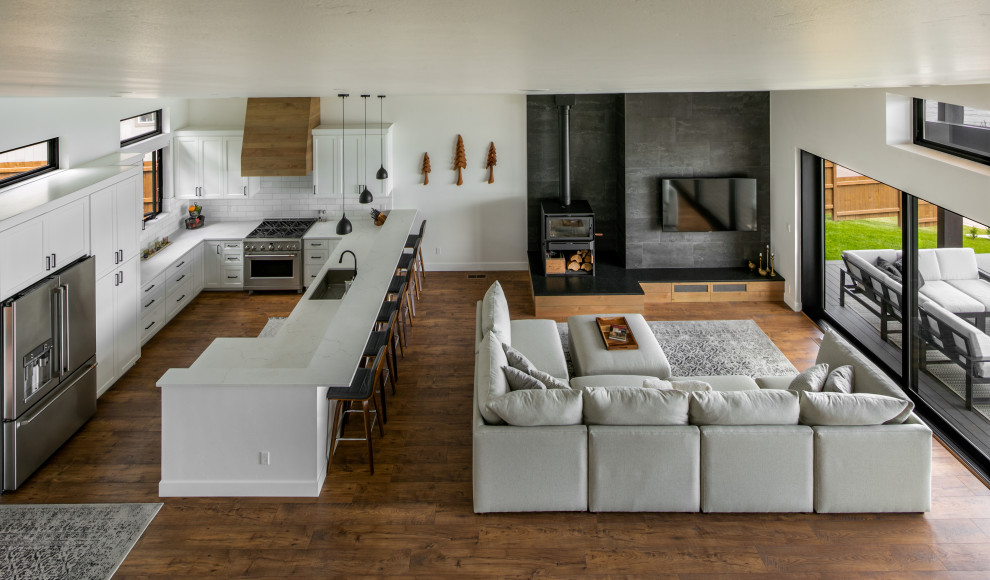 Immagine di un grande soggiorno moderno aperto con pareti bianche, pavimento in laminato, stufa a legna, cornice del camino piastrellata e pavimento marrone