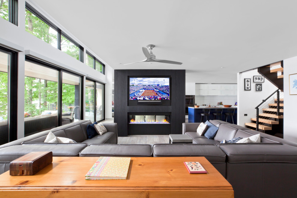 На фото: открытая гостиная комната среднего размера в стиле модернизм с домашним баром, белыми стенами, полом из винила, двусторонним камином, фасадом камина из дерева, телевизором на стене, серым полом и деревянными стенами