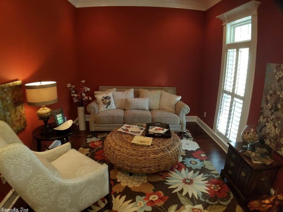 Cette image montre un petit salon craftsman fermé avec une bibliothèque ou un coin lecture, un mur rouge, parquet foncé, aucun téléviseur et un sol marron.