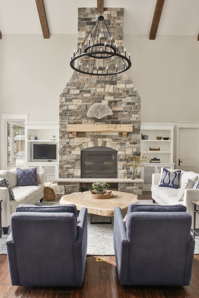 Cette image montre un grand salon traditionnel ouvert avec un mur gris, parquet foncé, une cheminée standard, un manteau de cheminée en pierre, un téléviseur encastré et un sol marron.
