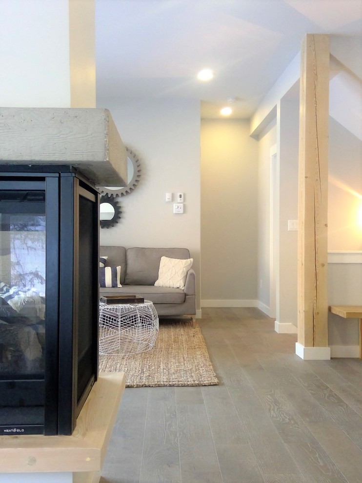 Immagine di un piccolo soggiorno stile marinaro aperto con pareti grigie, pavimento in legno massello medio, cornice del camino in cemento e pavimento grigio