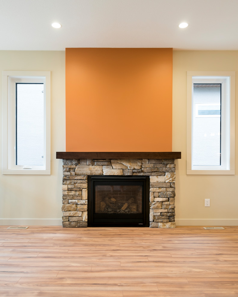 Пример оригинального дизайна: открытая гостиная комната в стиле модернизм с оранжевыми стенами, полом из ламината, стандартным камином, фасадом камина из камня, телевизором на стене и коричневым полом