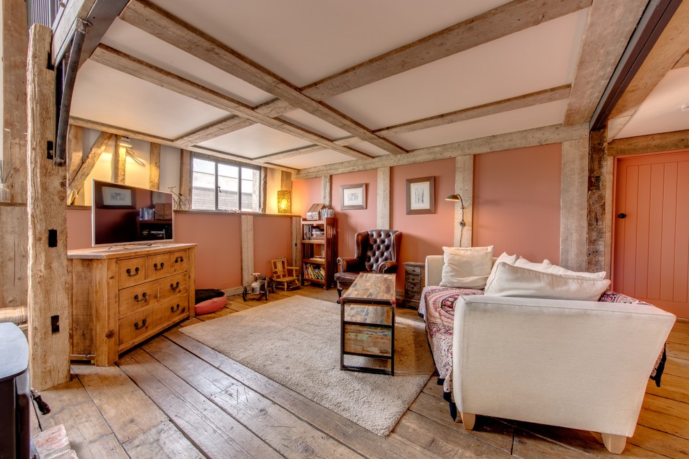 Modelo de salón para visitas abierto campestre con paredes rosas, suelo de madera en tonos medios y televisor independiente