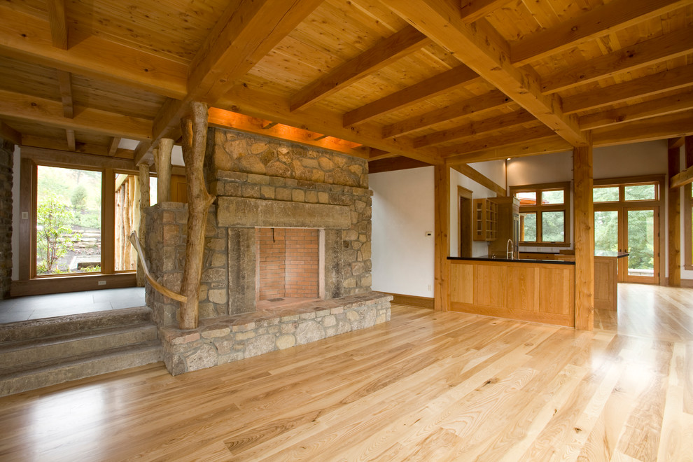 Ejemplo de salón abierto actual con paredes blancas, suelo de madera clara, chimenea de doble cara y marco de chimenea de piedra