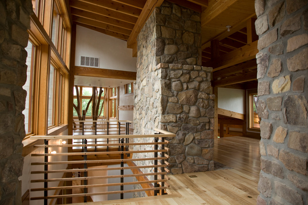 Imagen de salón abierto actual con paredes blancas, suelo de madera clara, chimenea de doble cara y marco de chimenea de piedra