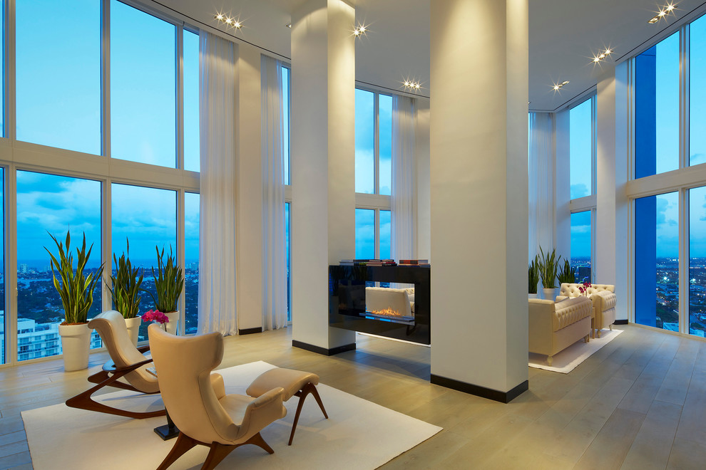 Großes, Offenes Modernes Wohnzimmer mit weißer Wandfarbe, hellem Holzboden, Kaminumrandung aus Stein und Tunnelkamin in Miami