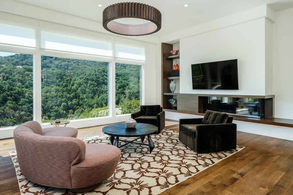 Стильный дизайн: открытая гостиная комната в современном стиле с коричневыми стенами, паркетным полом среднего тона, горизонтальным камином, фасадом камина из дерева, телевизором на стене и коричневым полом - последний тренд